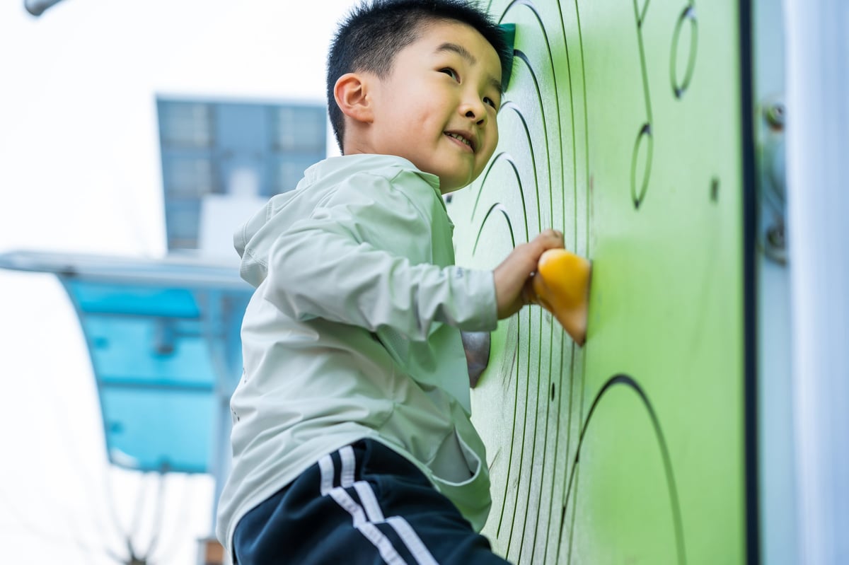 A young boy climbing a colorful climbing wall outdoors, engaged in active play